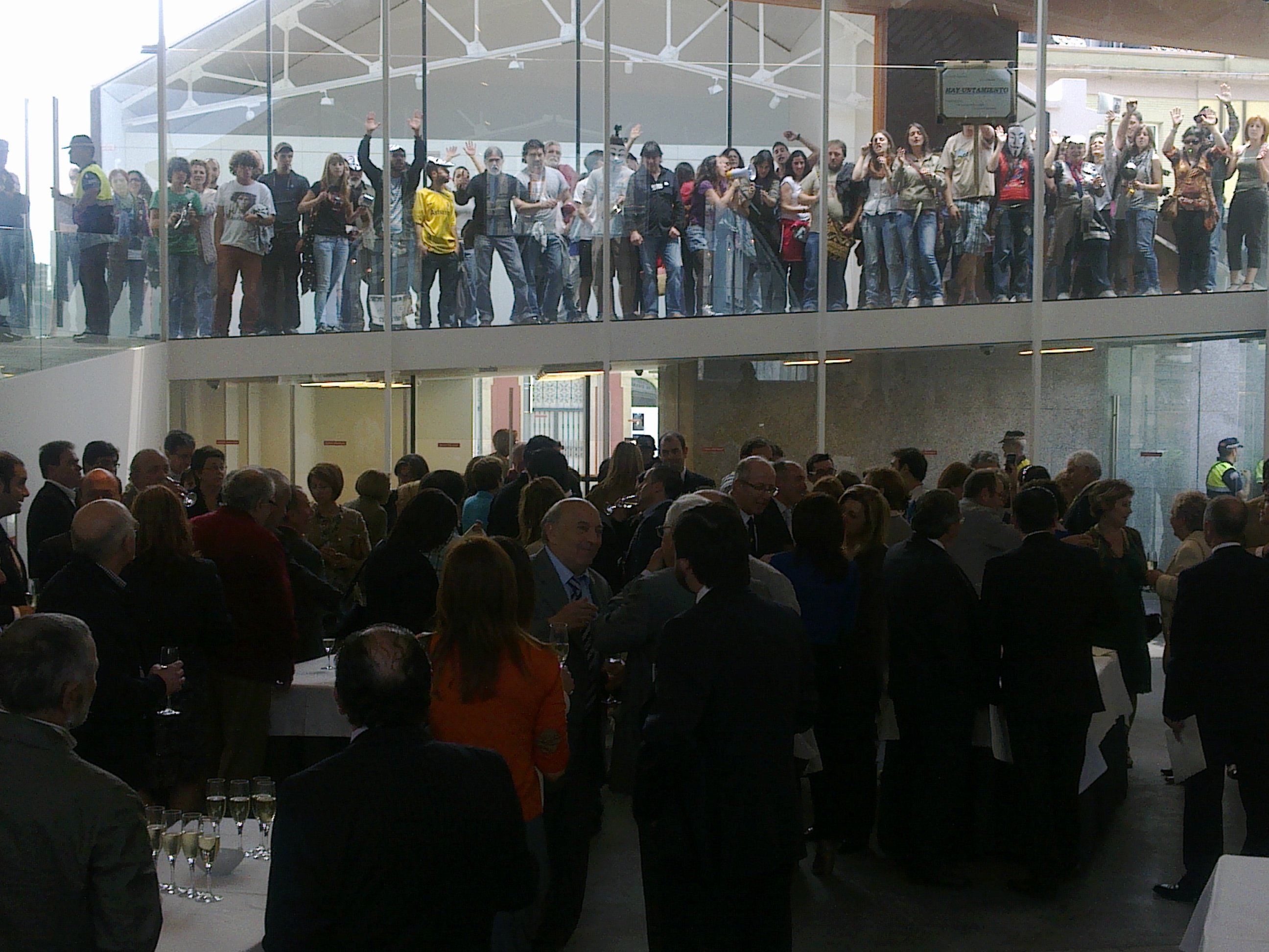 Local bigwigs toast with champagne after a local election in Avilas, Spain in 2011. Behind, the 'indignado' protesters have had enough