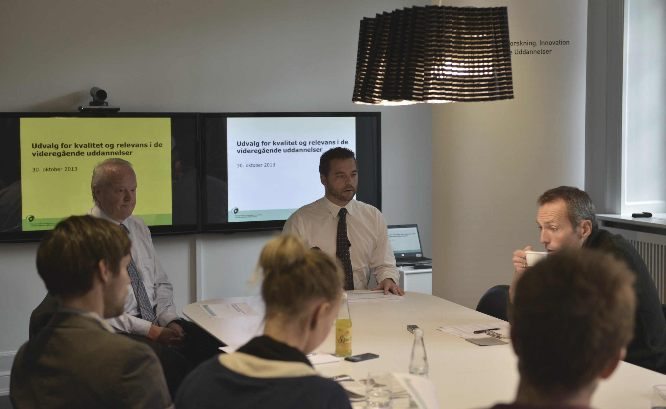 PRESSEMØDE - Udvalgsformand Jørgen Søndergaard foran den gule skærm flankeret af uddannelsesminister Morten Østergaard foran den hvide. I forgrunden th. slubrer Politikens udsendte en varm drik, mens det er Uniavisens gule sodavand cirka midt i billedet.