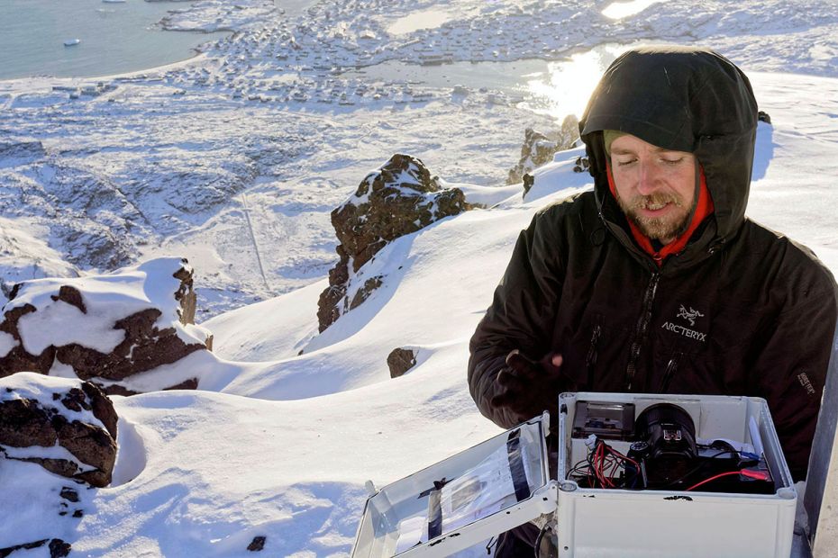 Three steps from where station leader Casper T. Christiansen is poised, lies an 800 metre drop. The small, Greenlandic city Qeqertarsuak lies in the ‘abyss’ in the background.