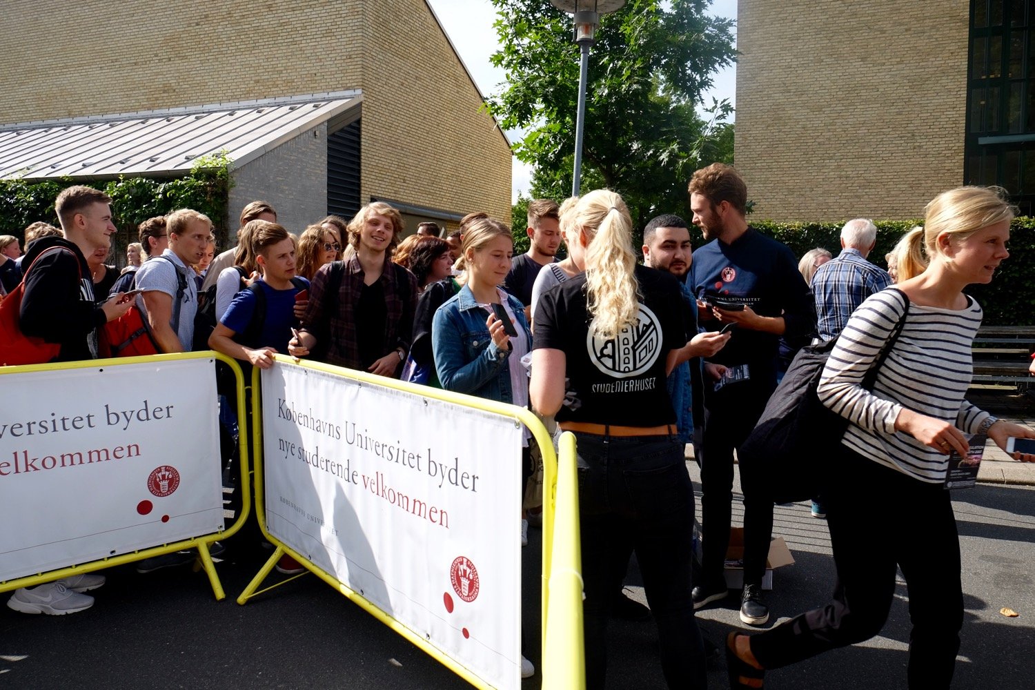 Hegnet er åbnet (dog ikke væltet) og de studerende strømmer hen mod indgangen. Til venstre joker en af de studerende med, at han skulle have taget en pressening med, så han kunne være sikker på at få en god plads. 