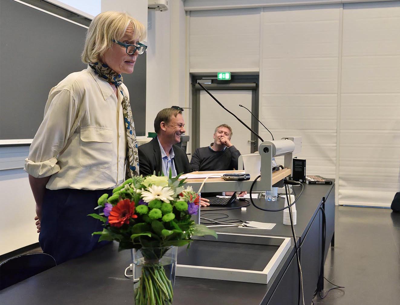 Mette Søltoft holder sit foredrag i auditoriet om fagets grundlægger - med et smil på alles læber. Bag Mette Søltoft sidder lektor Claus Valling Pedersen og lektor Rasmus Elling.