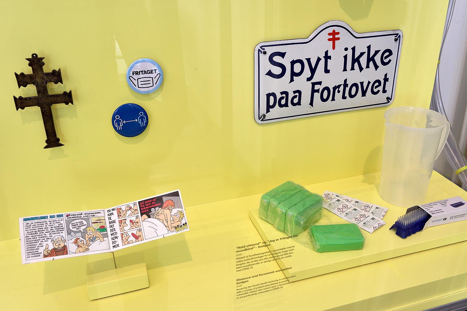 A cartoon with Oda and Ole, who had to learn how to have safe sex to avoid contracting AIDS. Above, there is a 'Keep your distance' badge for people who cannot wear a face mask or are particularly vulnerable to COVID-19. The enamel sign 'Do not spit on the pavement' was made to prevent the spread of tuberculosis.