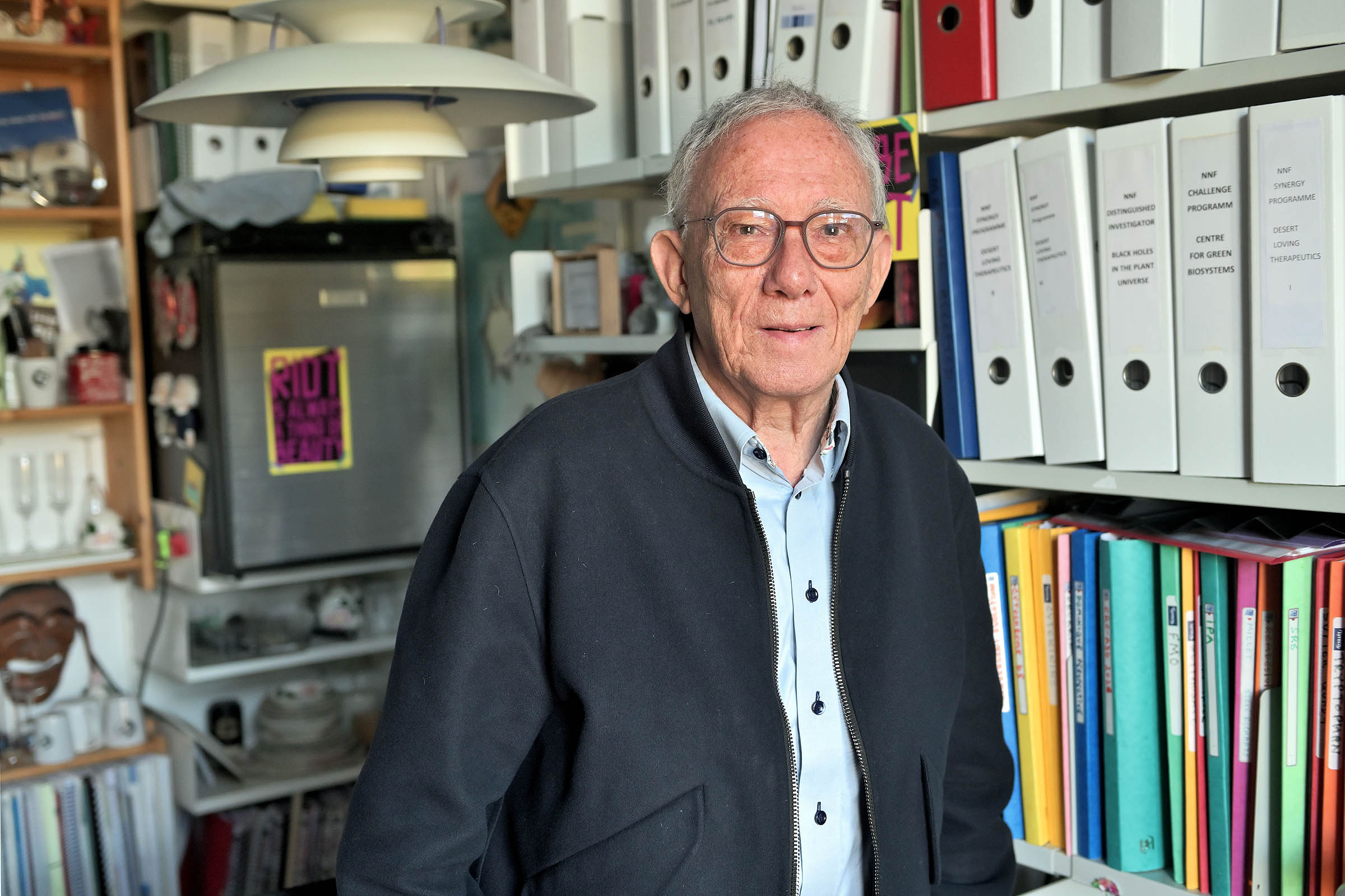 Professor Birger Lindberg Møller på sit hjemligt indrettede kontor på Institut for Plante- og Miljøvidenskab. Her er både minikøleskab og kaffemaskine, så han sparer tiden frem og tilbage til køkkenet. Den er bedre brugt på forskning, mener han.  